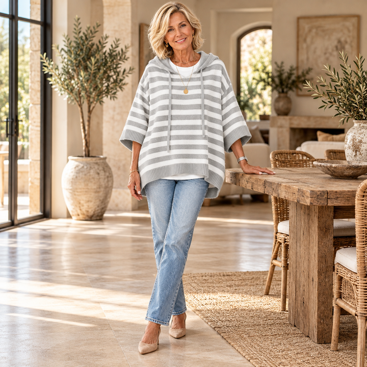Celine – Gray Striped Poncho Sweater worn by a mature blonde woman in a Mediterranean interior