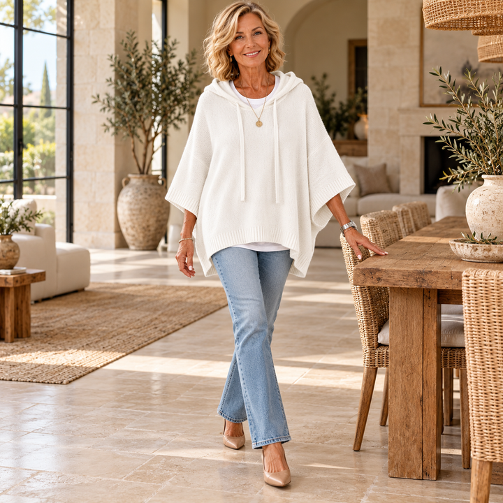 Janice – White Poncho Sweater worn by a mature blonde woman in a Mediterranean interior
